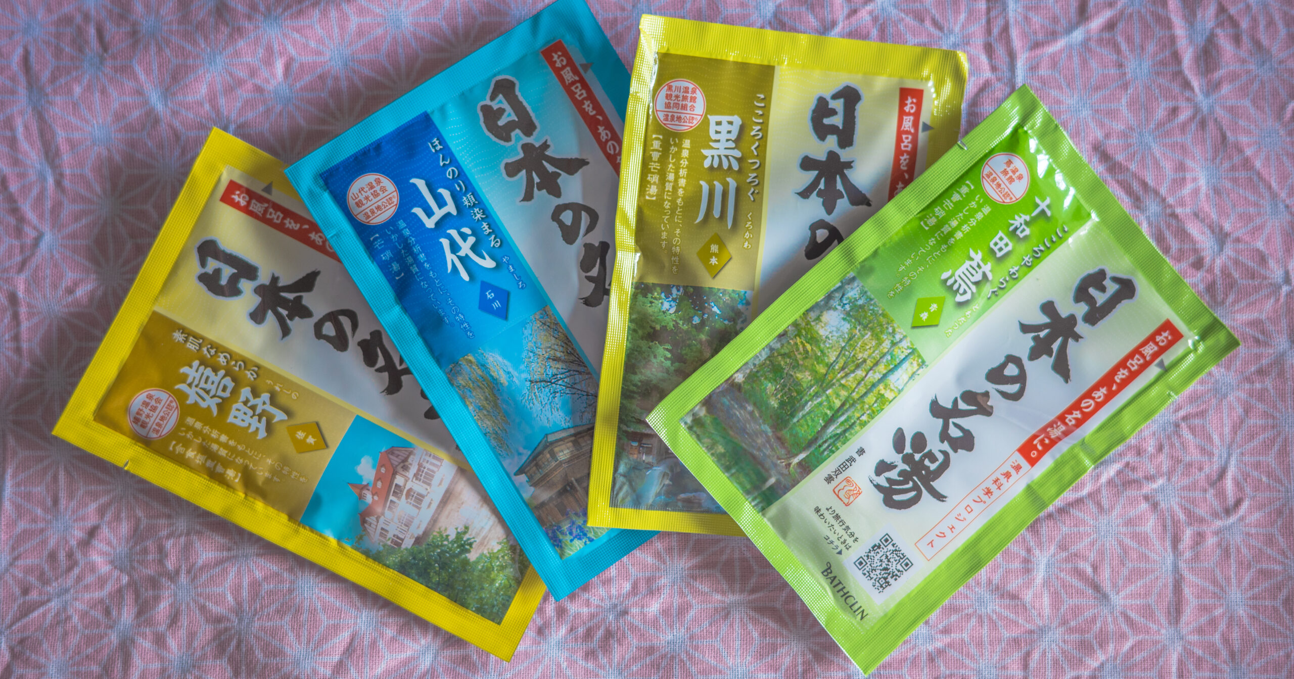 A hand pouring "Nihon no Meito" Japanese bath powder from a green sachet into bathwater, showcasing the relaxing moment at home.